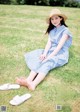 A woman in a blue dress and straw hat sitting on the grass.