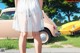 A woman in a white dress standing in front of a yellow car.