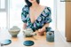 A woman sitting at a table with a teapot and cups.