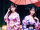 Two women in kimonos standing under an umbrella. 